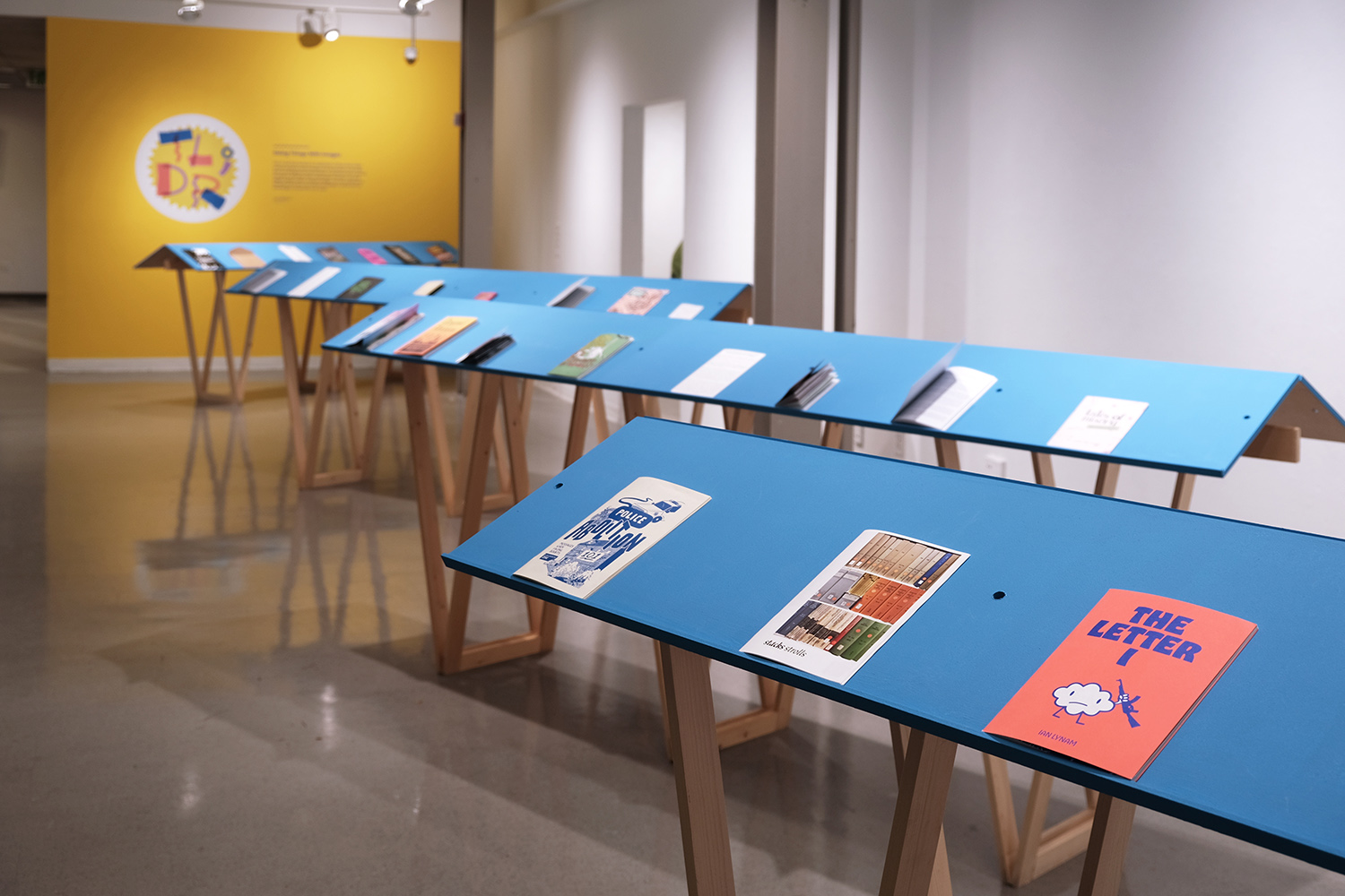 an image of an exhibition space with blue readers that have zines on them