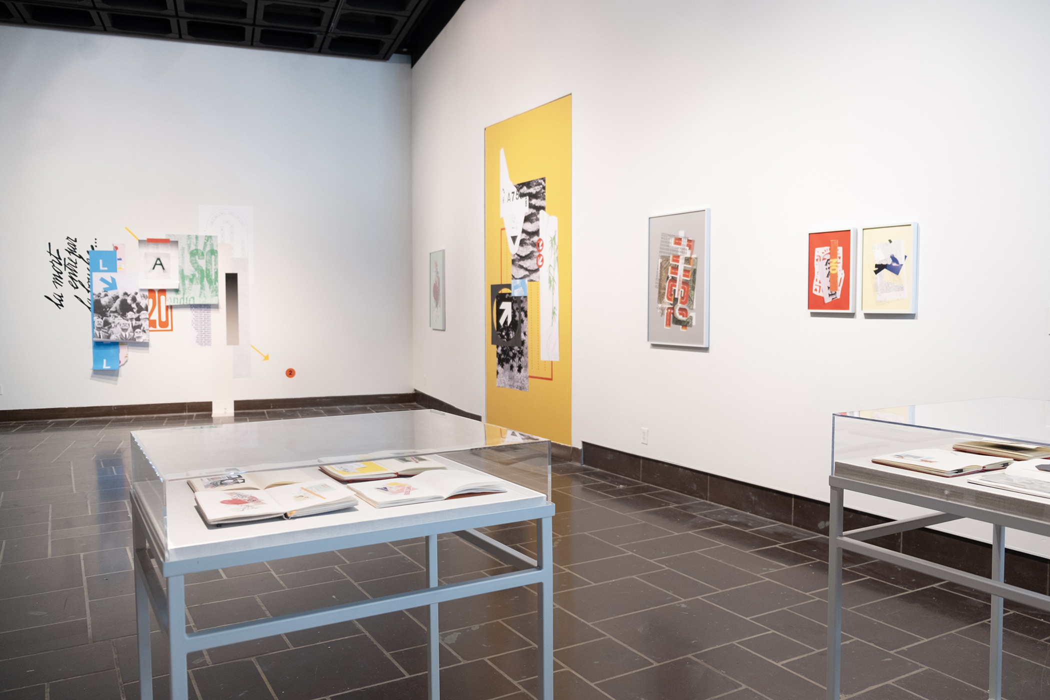 A gallery with large collages mounted directly to the walls and vitrines containing sketchbooks